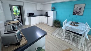 A modern kitchen with white cabinets, a microwave, and a refrigerator. There is a dining area with a table and chairs, and a blue wall with a plant and a picture.