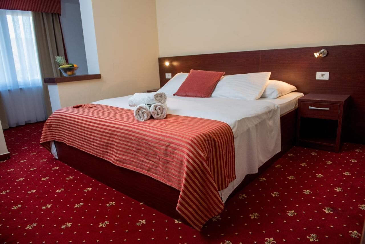 Habitación de hotel con una cama grande, cabecera de madera, mesita de noche y piso cubierto con alfombra roja.