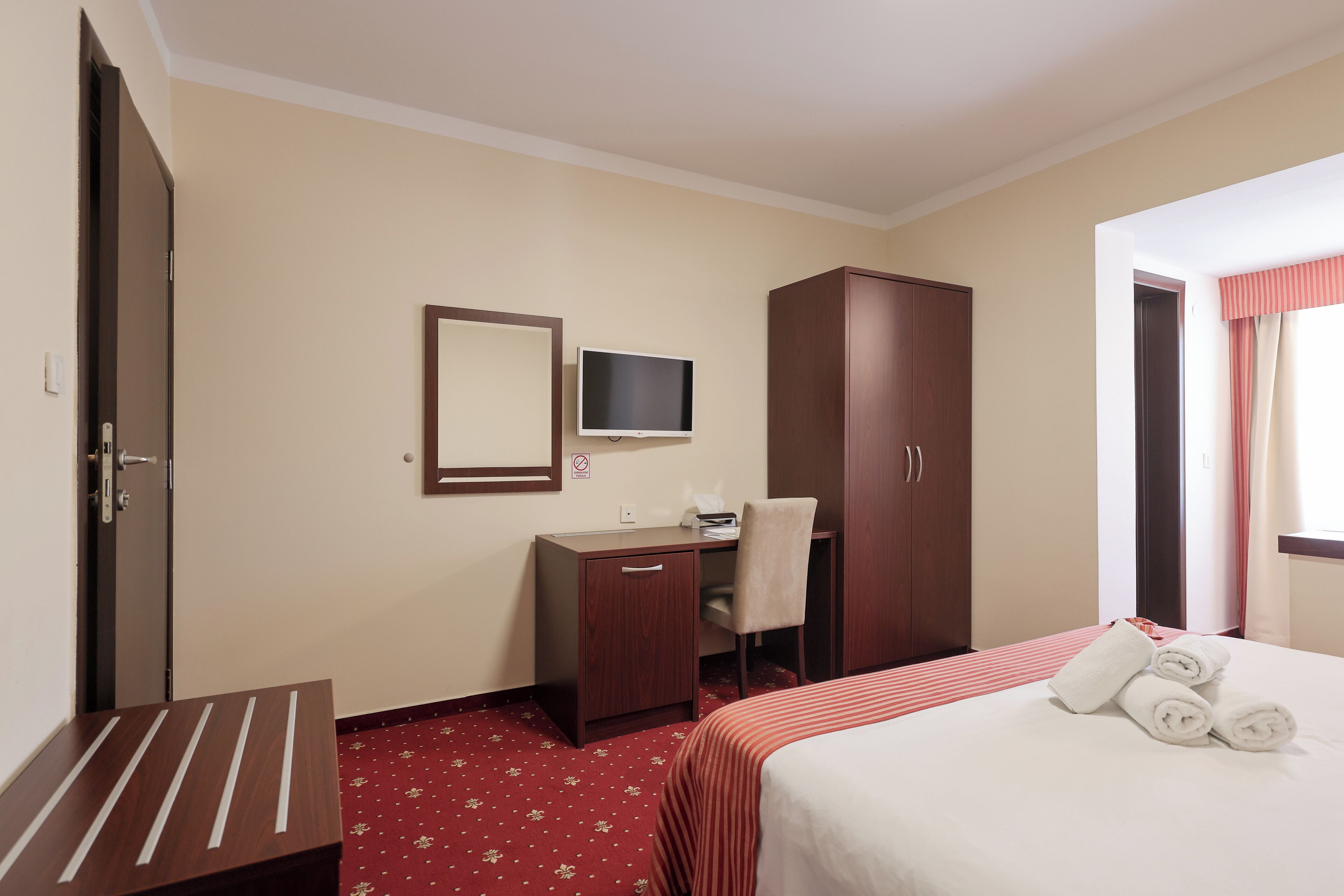 Una habitación de hotel con cama, escritorio, silla, televisor y armario.