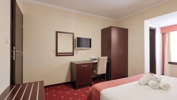 Una camera d'albergo con un letto, una scrivania, una sedia, una TV e un armadio.