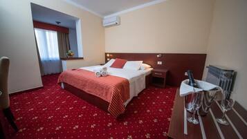 Une chambre d’hôtel avec un lit, une table de chevet sur laquelle se trouvent une bouteille et des verres, une chaise et une moquette rouge.
