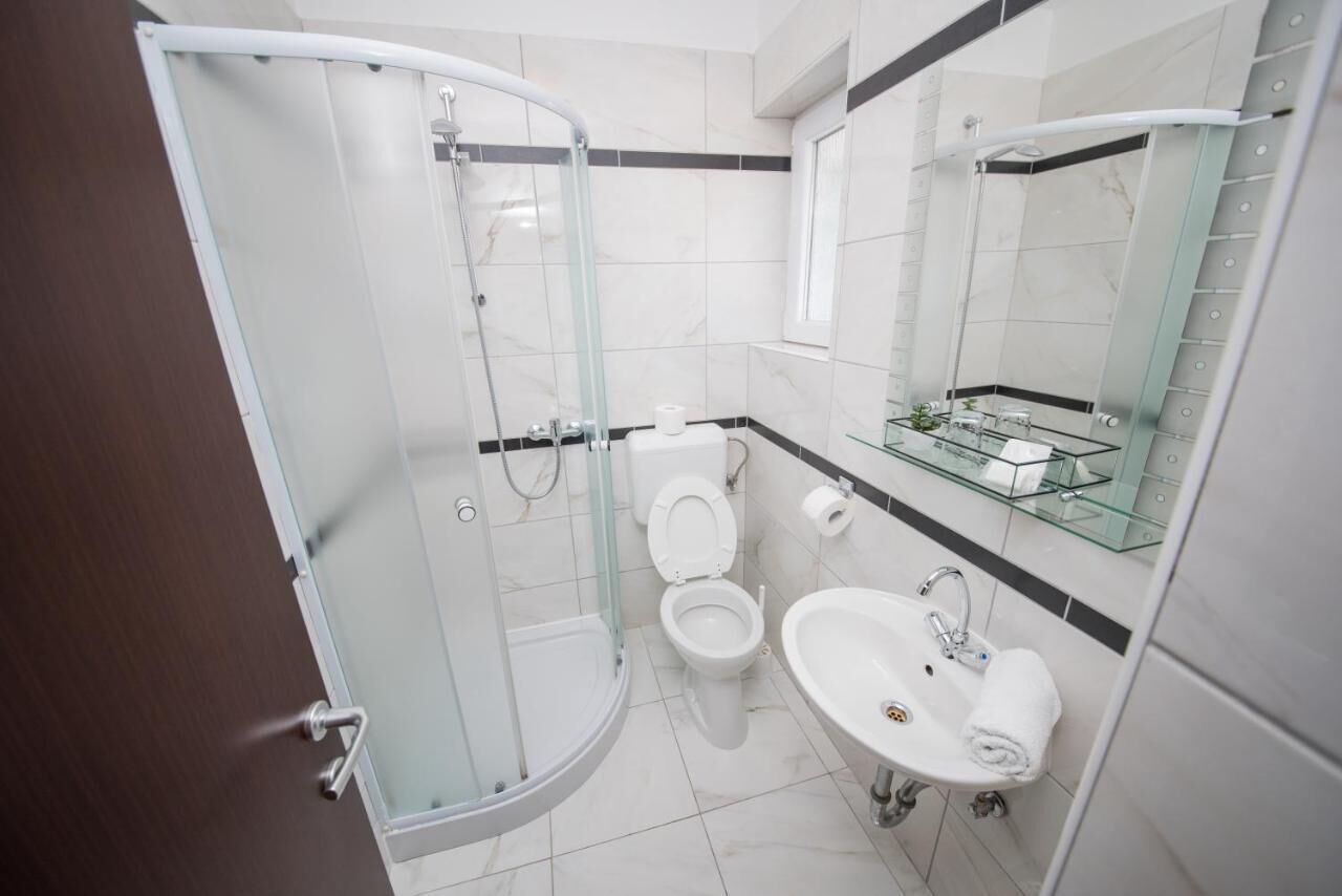 A modern bathroom with a glass-enclosed shower, a toilet, and a sink with a glass shelf above.