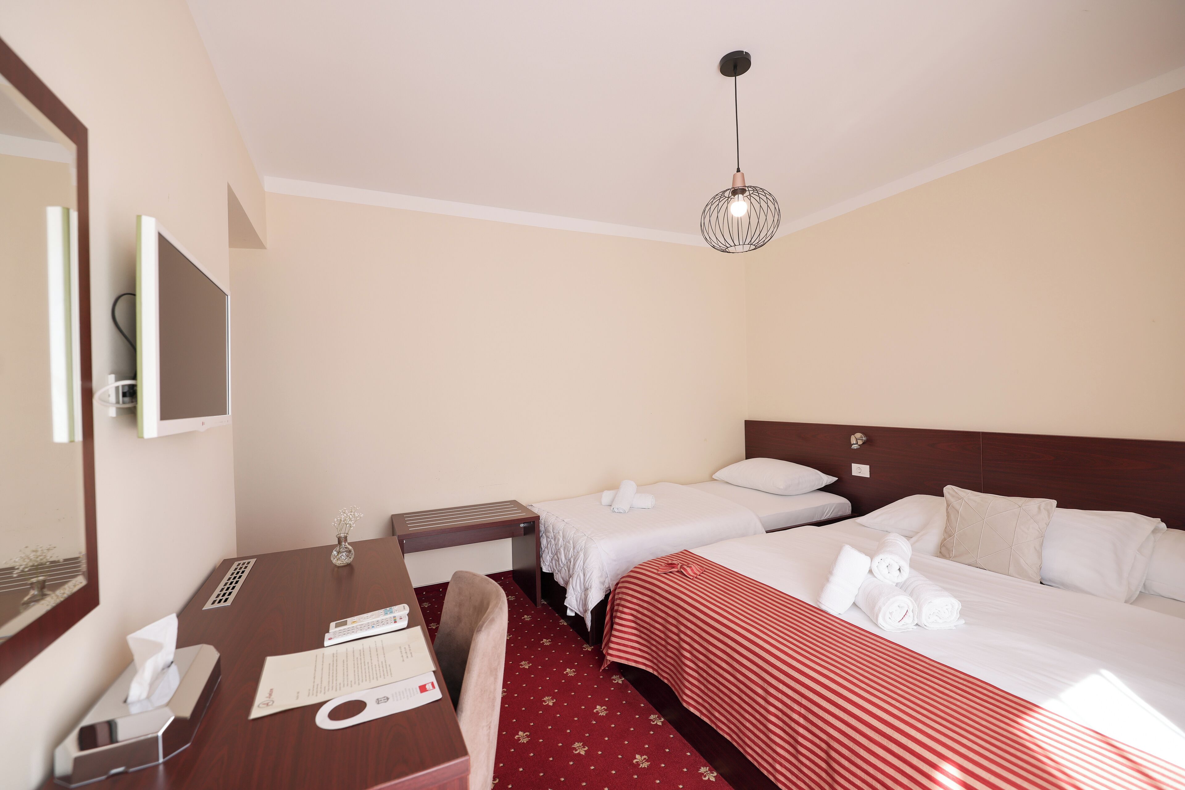 A hotel room with two beds, a desk with a telephone, a mirror, and a hanging light fixture.