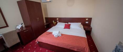 Una habitación de hotel con una cama grande, un armario, un escritorio y una mesita de noche.