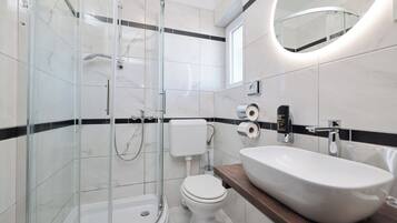 Un baño moderno con ducha envuelta en vidrio, inodoro blanco y un lavamanos grande tipo recipiente.