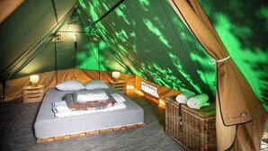 A tented accommodation with a bed, bedside lamps, a basket, and a view of trees through the fabric walls. - Huttopia Lagoa de Obidos  (Obidos)