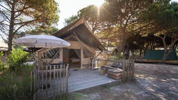 A wooden cabin with a thatched roof, a deck, and a table with chairs.