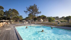 A swimming pool with wooden deck, lounge chairs, and umbrellas. - Huttopia Lagoa de Obidos  (Obidos)