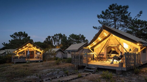 A series of tents with a wooden deck and seating area, surrounded by trees. - Huttopia Lagoa de Obidos  (Obidos)