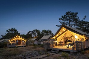 A series of tents with a wooden deck and seating area, surrounded by trees. - Huttopia Lagoa de Obidos  (Obidos)