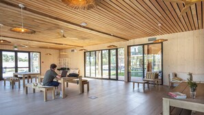 A spacious room with wooden floors, large windows, and a person working at a wooden desk. - Huttopia Lagoa de Obidos  (Obidos)