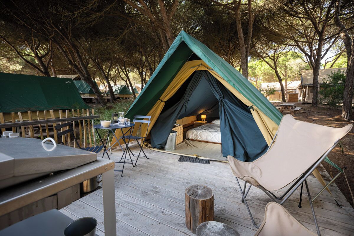 A tent with a bed inside, surrounded by a deck with a table and chairs.