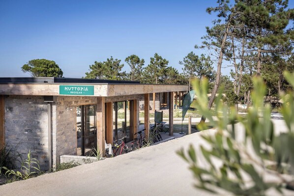 A building labeled "HUTTOPIA - RECEÇÃO" with a covered outdoor area, bicycles, and a clear sky. - Huttopia Lagoa de Obidos  (Obidos)