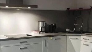 Una cocina moderna con armarios blancos, un lavamanos de acero inoxidable y una cafetera.