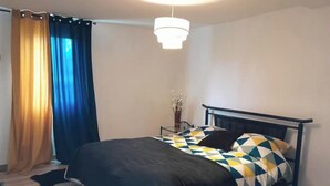 Un dormitorio con cama, mesita de noche, lámpara y ventana con cortinas.