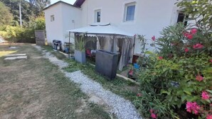 Una casa con un espacio exterior techado, un sendero de grava y un jardín con flores rosadas.