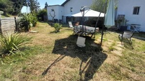 Patio trasero residencial con una mesa y sillas, rodeado por una casa blanca con un área de estar al aire libre techada.