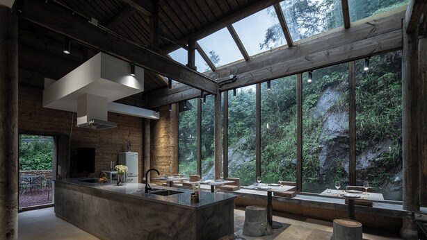 Una cucina moderna con un'isola grande, travi in legno e ampie finestre che si affacciano su una zona boschiva.