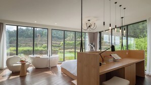 Una camera da letto moderna con un'ampia finestra, una scrivania in legno, una vasca da bagno bianca e una sedia bianca.