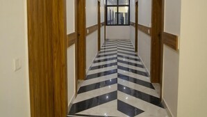 A hallway with a checkered floor pattern, wooden doors, and recessed lighting. - Serenity By The Ganges (Haridwar)