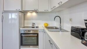 Eine kleine Küche mit weißen Schränken, einem Einbauofen, einer Spüle und einem Wasserhahn sowie einem Toaster.