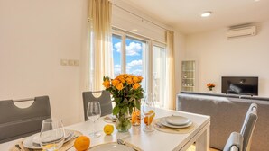 Ein Essbereich mit einem Tisch für zwei Personen, einer Blumenvase und Blick zum Himmel durch große Fenster.