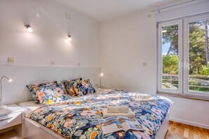 Ein Schlafzimmer mit Bett, Nachttischen, einer Lampe und einem Fenster mit Blick auf Bäume.