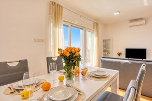 Un comedor con una mesa dispuesta para dos, un florero con flores y un televisor al fondo.