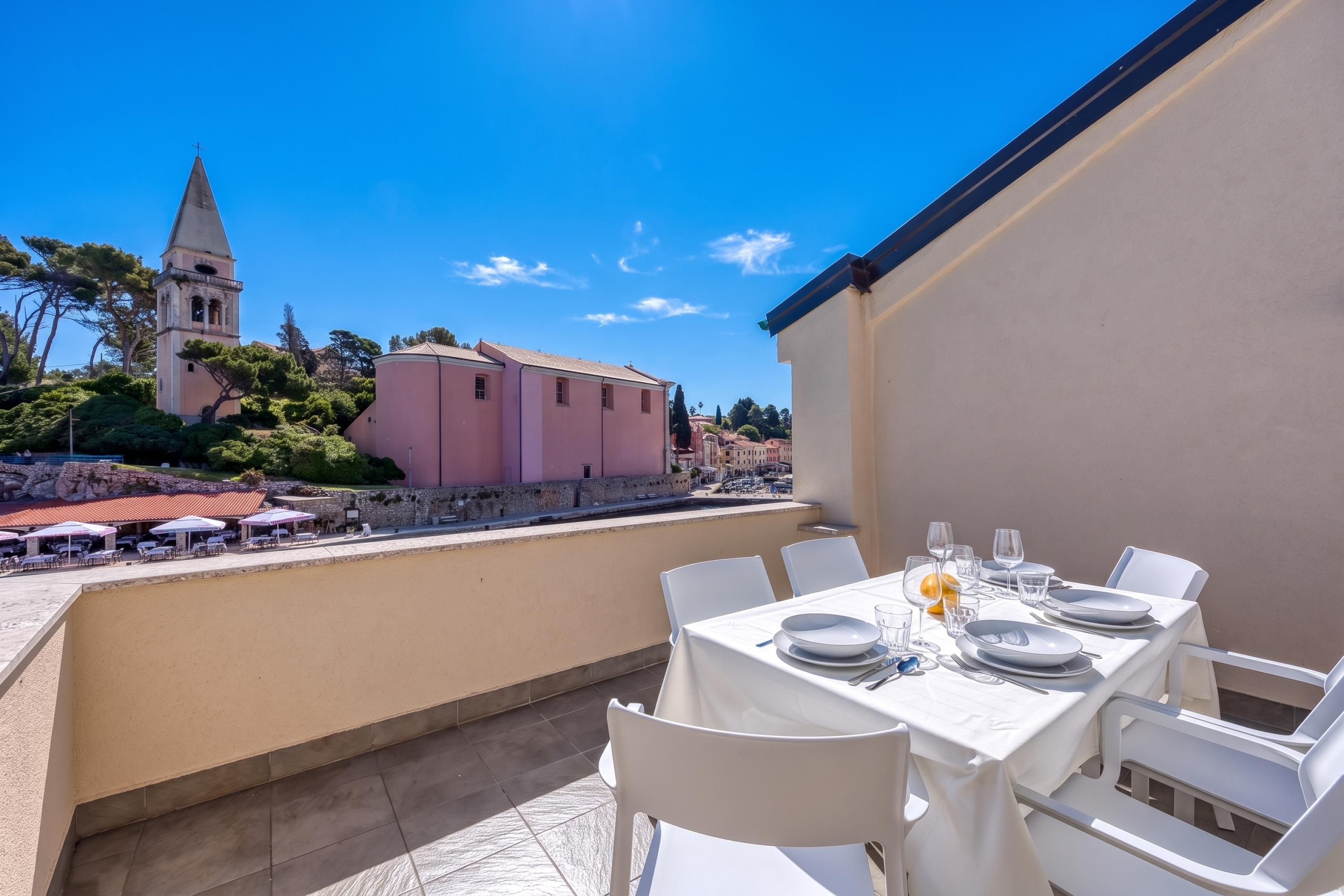 Une terrasse avec une table dressée pour le dîner, offrant une vue sur une ville historique avec une église et des bâtiments aux façades roses.