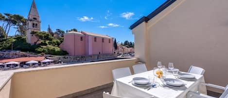 Una terraza con mesa lista para comer, con vistas a un pueblo histórico con una iglesia y edificios de color rosa.
