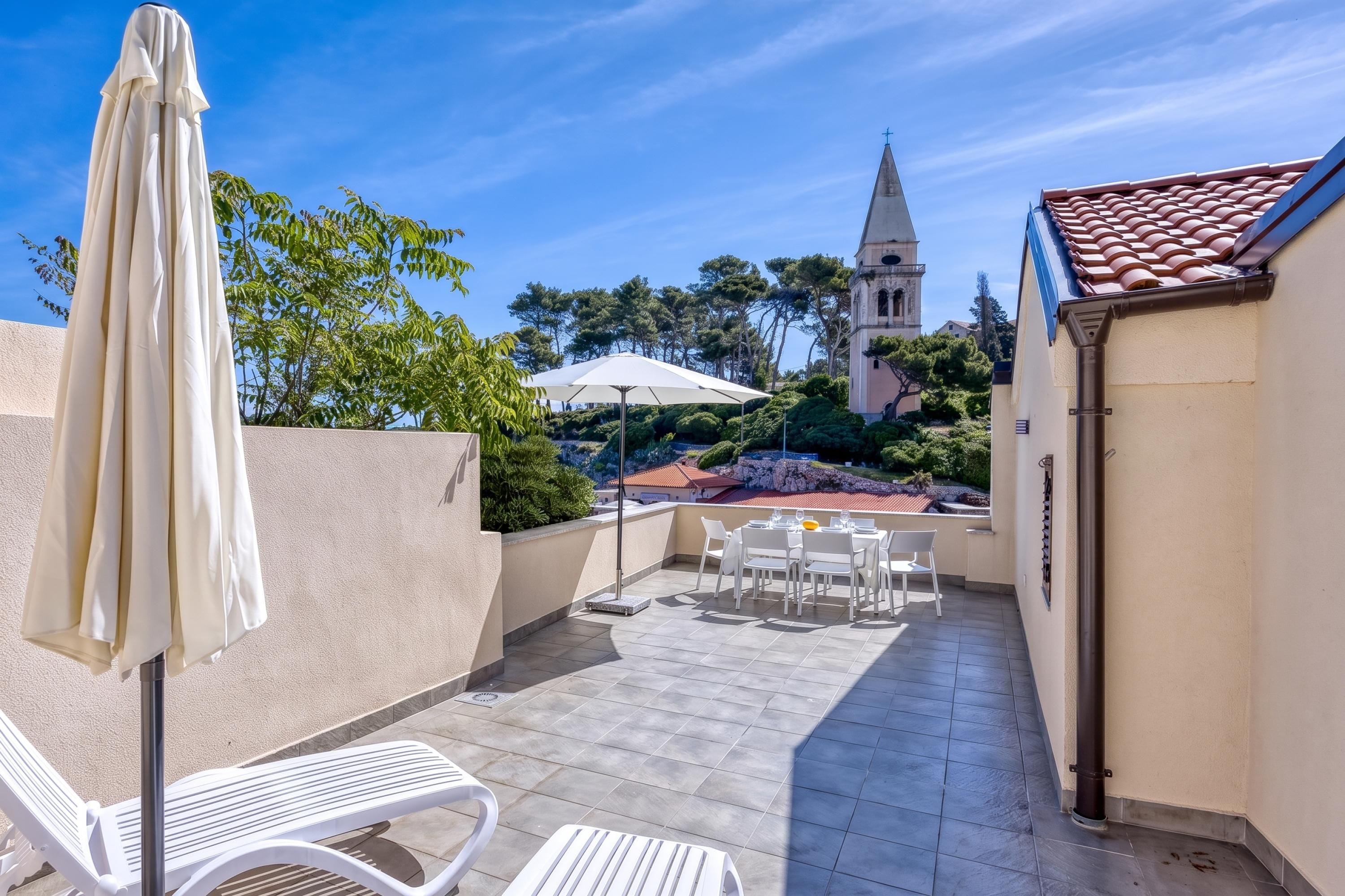 A rooftop terrace with outdoor seating, a white umbrella, and a view of a church tower.