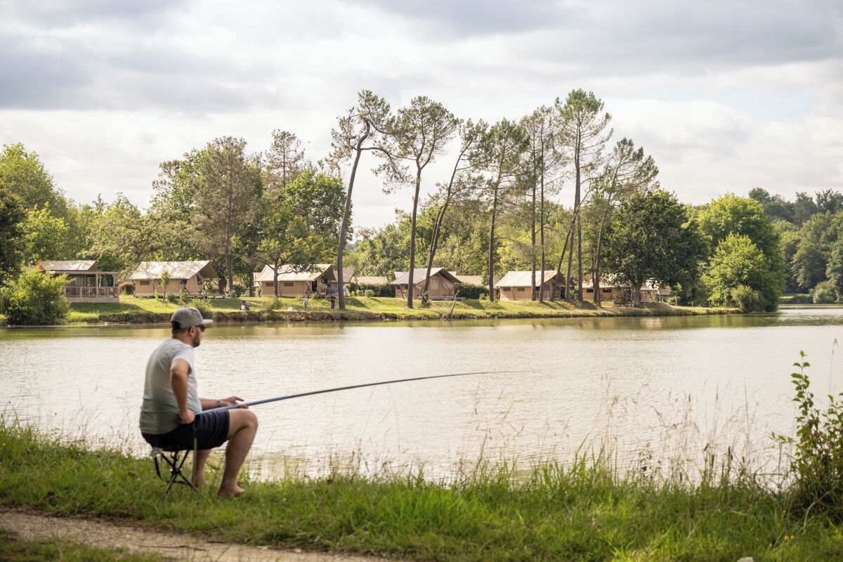 Un homme est en train de pêcher au bord d’un lac paisible, avec des maisons en arrière-plan.
