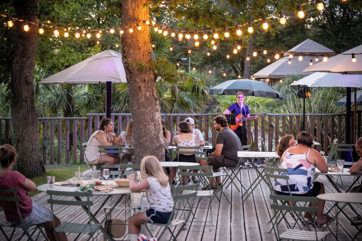 An outdoor dining area with tables and chairs, string lights, and umbrellas.