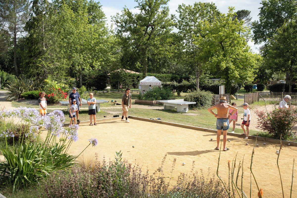 Eine Gruppe spielt Boccia auf einem Sandplatz im Freien, umgeben von Grünflächen und Bäumen.