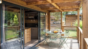 Een houten terras met een eettafel, een schuifdeur naar een keuken en uitzicht op de omgeving.