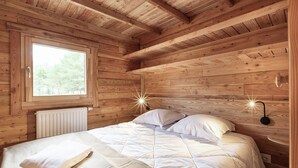 Een slaapkamer in een houten chalet, met een bed, een raam en een wandlamp.
