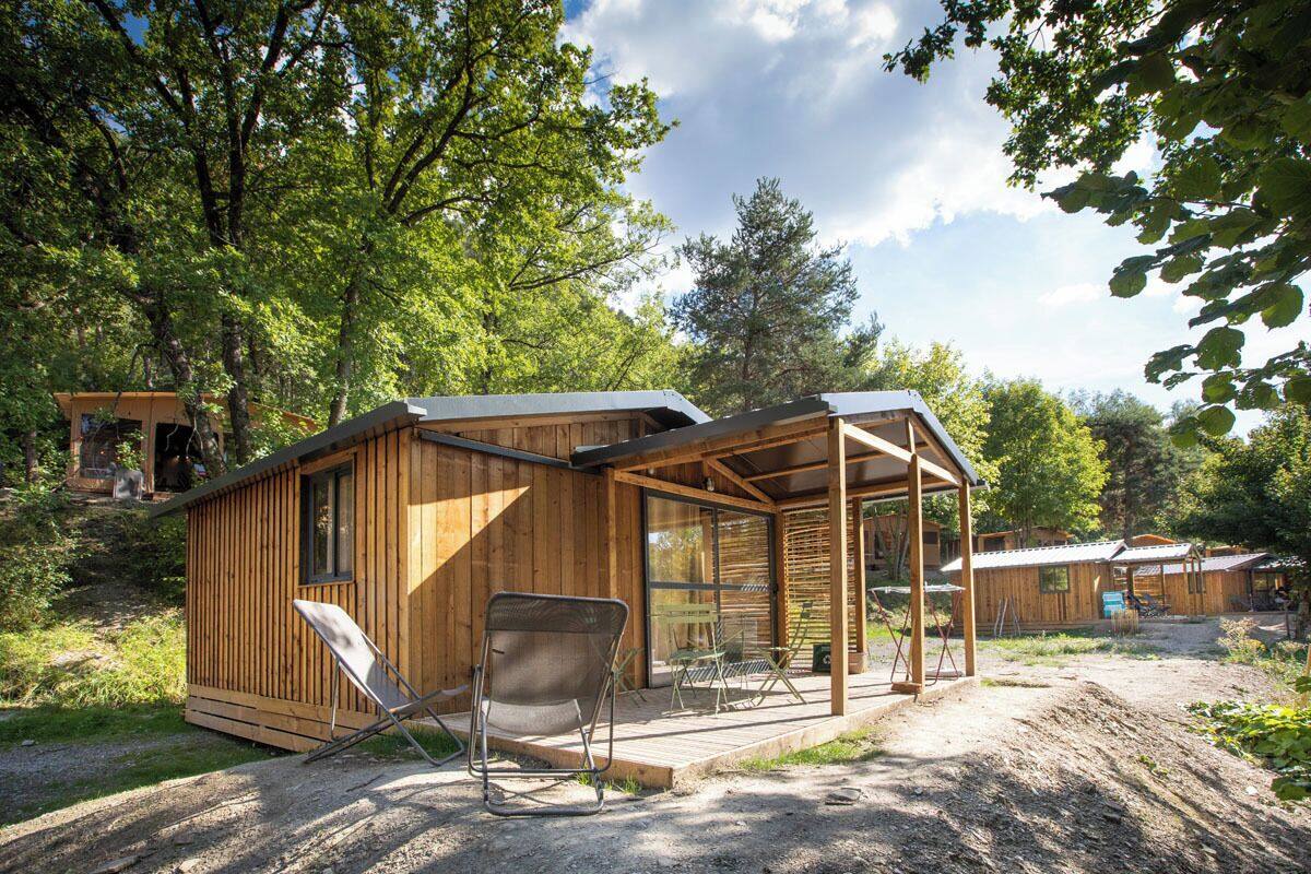 A wooden cabin with a glass door entrance, a patio with a chair, and a small deck area.