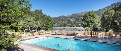 A swimming pool with lounge chairs and a wooden deck, surrounded by trees and mountains in the background.