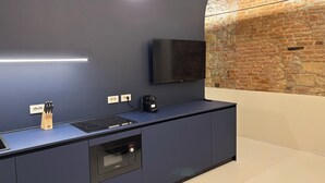 A modern kitchen with a built-in oven, a coffee machine, and a flat-screen TV mounted on the wall.