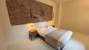 A modern bedroom with a stone wall, a bed with white bedding, and two bedside tables with lamps.