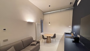 A modern living room with a sofa, a round table, and chairs. There is a radiator, a window, and a black wall with a whiteboard.
