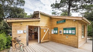 A wooden cabin with a wooden deck, a bicycle, and a sign reading "HUTTOPIA ACCUEIL". - Huttopia Oléron les Chênes Verts  (Dolus-d'Oléron)
