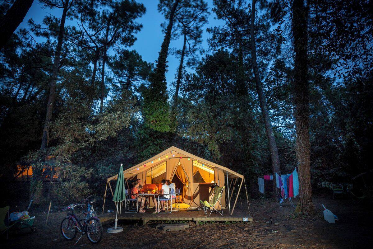 A tented accommodation in a forest with a dining area and bicycles.