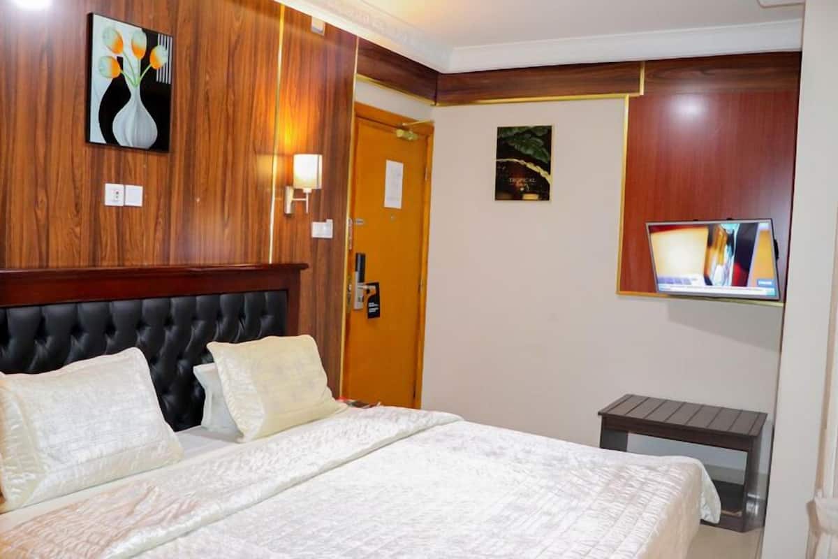 A hotel room with a large bed, a wooden headboard, a painting on the wall, a television mounted on the wall, and a small wooden table.