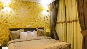 A hotel room with a bed, patterned wallpaper, a nightstand, a lamp, and curtains.
