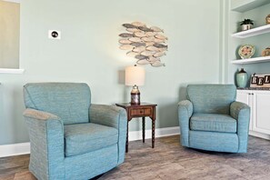 Two armchairs, a small table with a lamp, and a decorative wall piece in a room with light green walls and wooden flooring. - Escape to Sunset Serenity, a spacious 4BR 3BA retreat in beautiful Sunset Beach, NC. (Sunset Beach)
