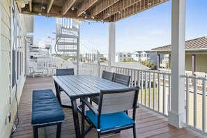 A covered outdoor deck with a table and chairs, a spiral staircase, and a view of neighboring houses. - Escape to Sunset Serenity, a spacious 4BR 3BA retreat in beautiful Sunset Beach, NC. (Sunset Beach)