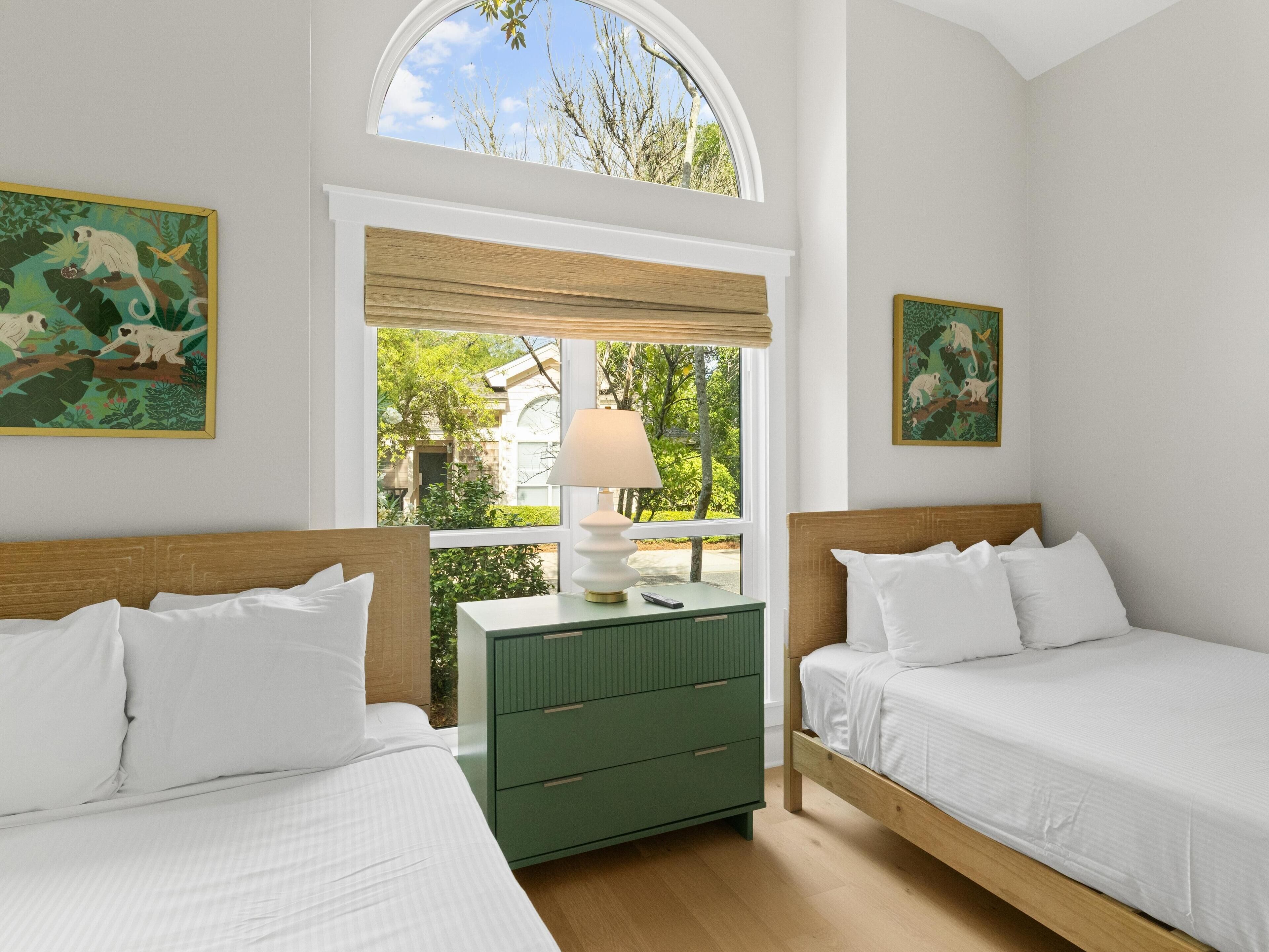 A bedroom with two beds, a green dresser, a window with a view of greenery, and two animal-themed wall paintings.