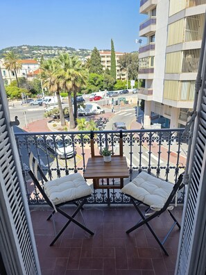 A balcony with a table and two chairs, overlooking a street with cars and buildings. - Lovely 2-bedroom apartment in Cannes 5mn walk to Croisette (Cannes)