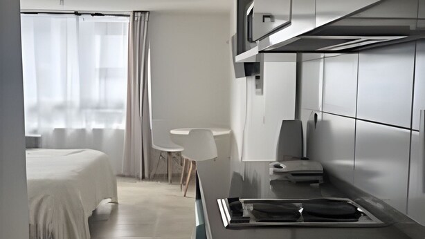 A modern, minimalist hotel room with a bed, a small table, a chair, a kitchenette, and a window with sheer curtains. - Hermoso estudio en Santiago (Santiago)